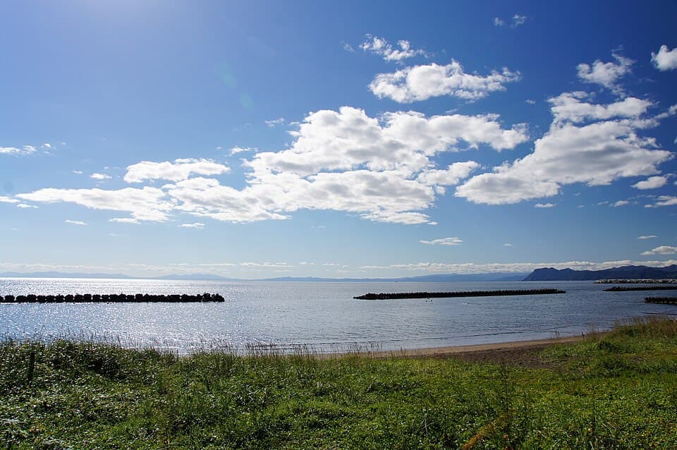 青空と雲の下に広がる海、海岸の草地と防波堤